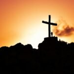 Majestic silhouette of a cross on a hill during a vivid sunset, symbolizing spirituality.